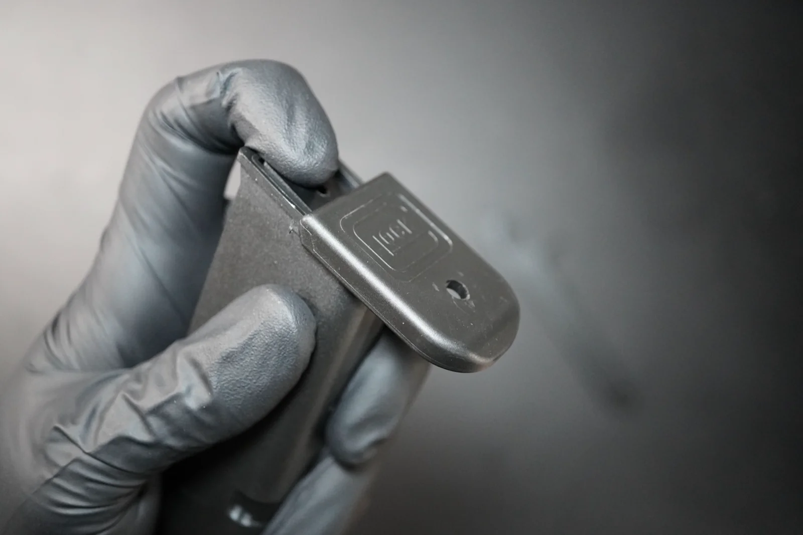 Gloved fingers controlling the floor plate as it slides off a Glock magazine, holding the spring in to keep it from launching out